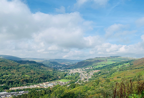 A valley seen from the air. The sky is bright and the rolling hills are a lush green.)