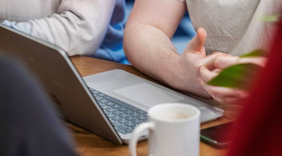 A laptop and coffee cup with view of team workers discussing the 2025 digital switchover. 